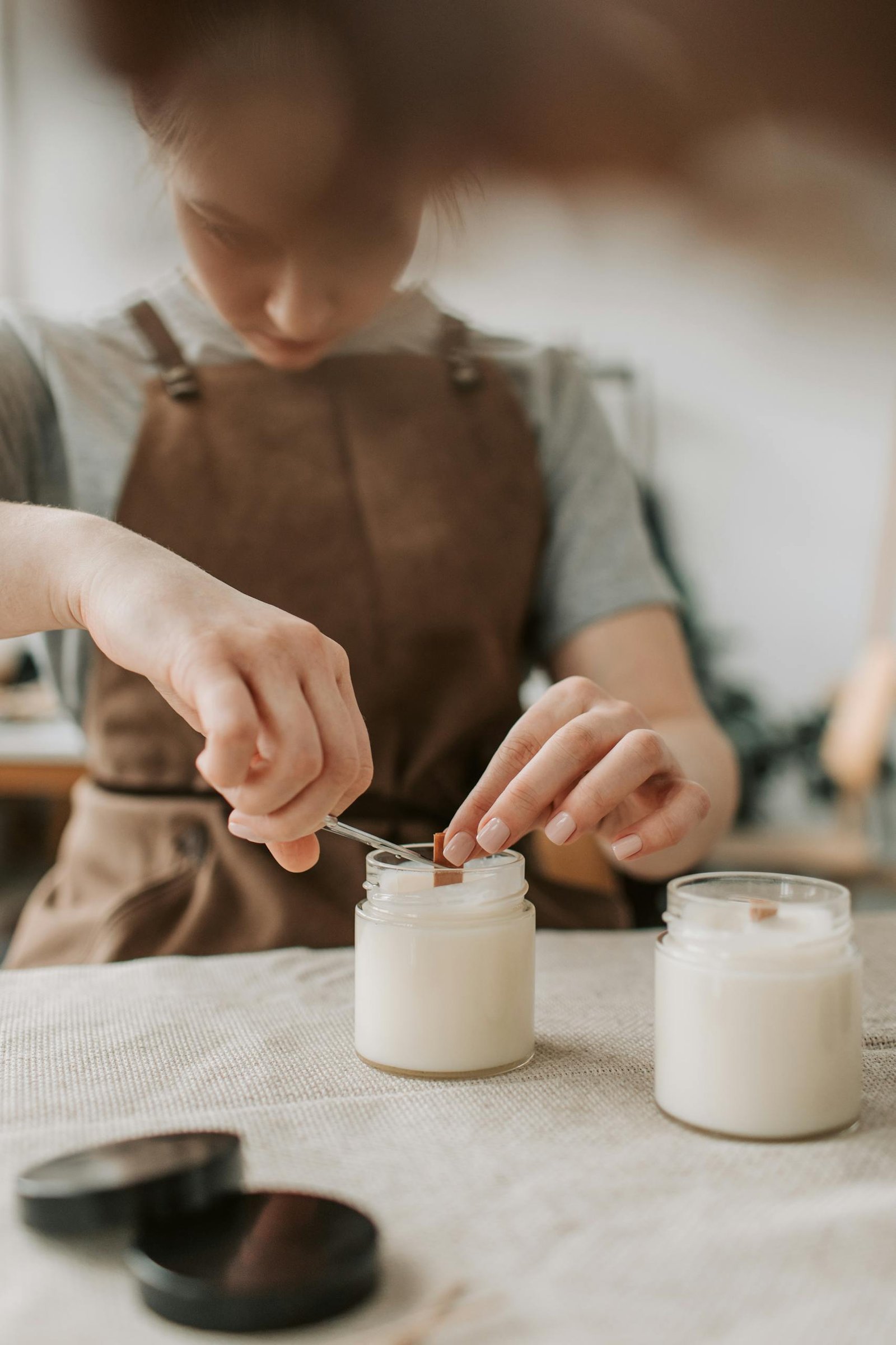 A woman carefully crafting handmade soy candles in an artisanal workshop setting.